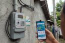 Warga mengecek promo tambah daya 50 persen di PLN Mobile dekat meteran listrik rumah.(ilustrasi poto: AI).