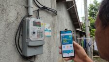 Warga mengecek promo tambah daya 50 persen di PLN Mobile dekat meteran listrik rumah.(ilustrasi poto: AI).