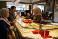 Pelayan toko emas di Jambi menunjukkan kalung perhiasan kepada pembeli di depan etalase berkilau penuh perhiasan.(poto: jemarionline.com).
