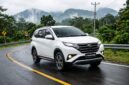 Ilustrasi Daihatsu Terios putih melaju mulus melintasi jalanan aspal berkelok di kawasan perbukitan yang hijau dan berkabut tebal.(poto: AI).