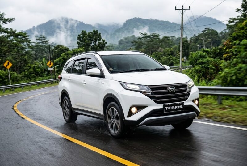 Ilustrasi Daihatsu Terios putih melaju mulus melintasi jalanan aspal berkelok di kawasan perbukitan yang hijau dan berkabut tebal.(poto: AI).