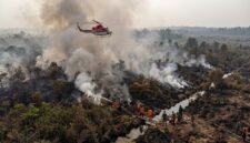 Ilustarsi Petugas gabungan membasahi lahan gambut Jambi di bawah kepulan asap pekat, sementara helikopter bom air siap beroperasi.(poto: AI).