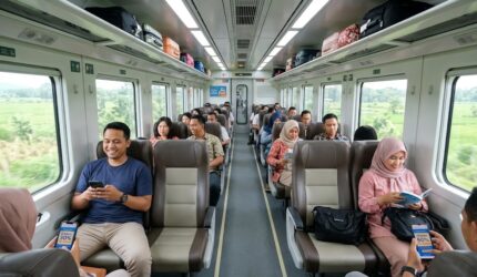 Ilustrasi Penumpang menikmati perjalanan di gerbong kereta api ekonomi berpenyejuk udara dengan kursi lapang.