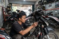 Ilustrasi: Mekanik sedang memasang sistem kunci keyless pada motor bebek di sebuah bengkel modifikasi di Jakarta.(poto: AI).